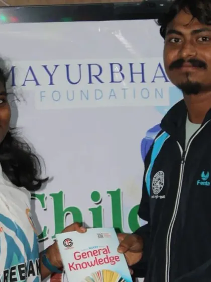 A young girl receives a general knowledge book as a prize. Our Children's Day events often include educational components like quizzes and essay competitions to promote learning.