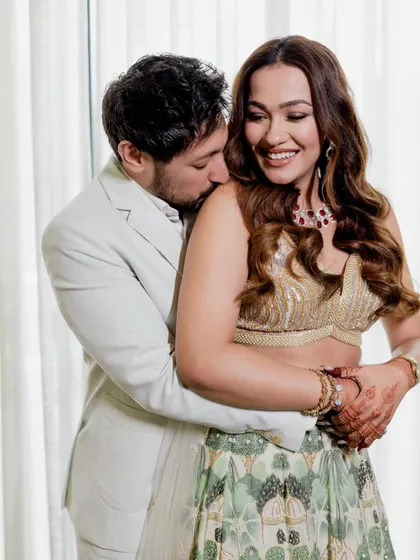A tender and romantic moment from an engagement shoot, with the groom embracing the bride from behind and kissing her shoulder.