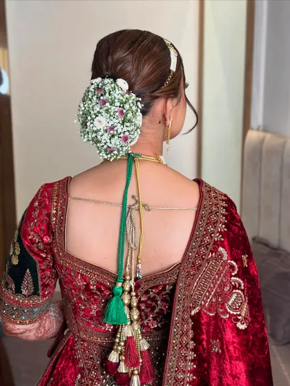 This bridal bun is adorned with a full gajra of baby's breath and small pink flowers, creating a delicate and ethereal look for the bride's special day.