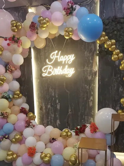 A closer look at the pastel balloon arch with a "Happy Birthday" neon sign. This setup is versatile and can be adapted for various spaces, including restaurants and small halls.