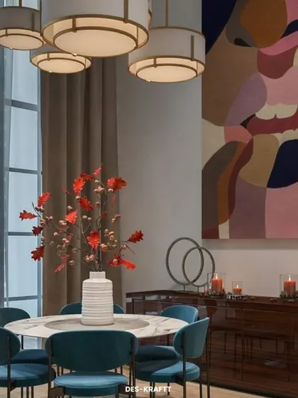 A bold and artistic dining room featuring a marble-topped table, deep teal velvet chairs, and a large, colorful abstract painting that serves as a dramatic focal point.