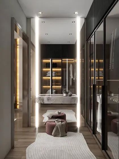 A long, galley-style walk-in closet with glass-fronted wardrobes on one side and a vanity on the other. The vertical strip lighting makes the space feel taller and more dramatic.