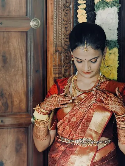 A close-up of the bride adjusting her jewelry, showing the intricate details of her henna and the flawless makeup.