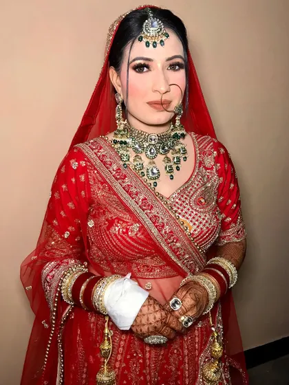 A full-length view of Sonia's bridal attire. The coral-red lehenga is beautifully complemented by the soft, radiant makeup.