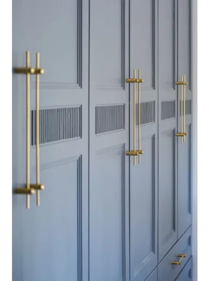A close-up of the custom brass handles on a grey wardrobe. The design includes a small fluted detail, adding a subtle texture that elevates the entire piece.