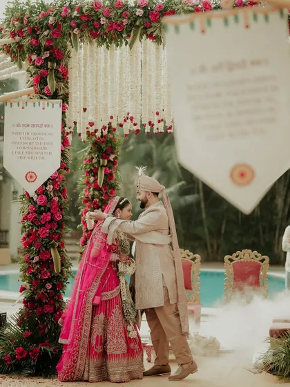 The groom lovingly places the garland around his bride, a tender moment of acceptance and union. The soft smoke and floral decor create a dreamy, romantic setting.