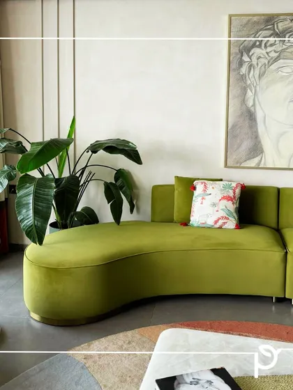 A large Bird of Paradise plant complements the green curved sofa and artistic decor in this modern living space. Using large statement plants is a great way to make a bold design impact and bring life to interiors.