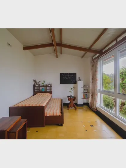 Designed as a simple retreat, this room in 'Malenadu Mane' features a large window with stunning views of the green landscape. The furniture is functional and understated, keeping the focus on the natural surroundings.