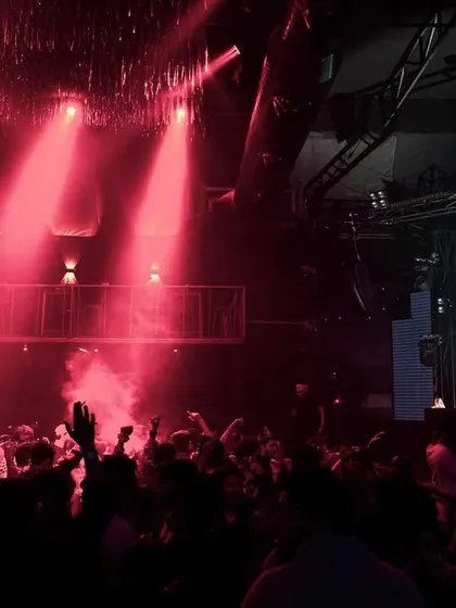 The crowd at Elrow with their hands up, silhouetted against the red lights and stage visuals.