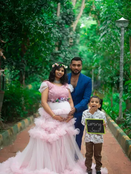 A happy family maternity shoot in the park. The mom-to-be is in a pink ruffle gown, and her son holds a 'Coming Soon' sign, making it a memorable announcement.