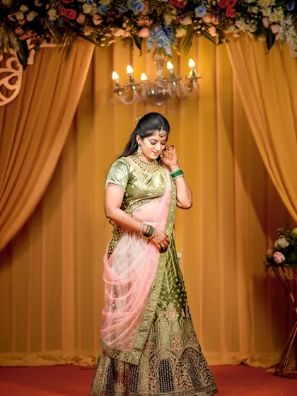 A full-length portrait of the bride, showcasing her green and pink lehenga and the elegant reception decor.