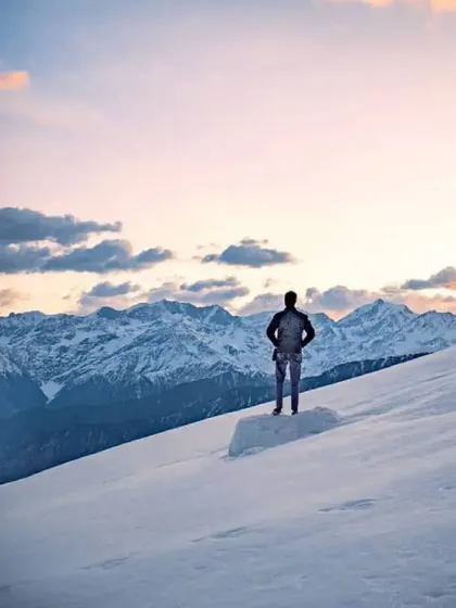 A lone trekker gazes at the majestic Himalayan range from a snow-covered ridge on the Brahmatal trek. This is the reward for a hard climb: solitude and a view that touches the soul.