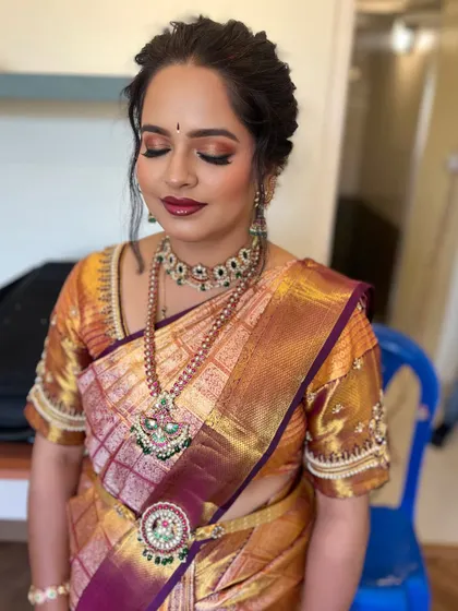 A classic South Indian bridal look with a beautiful gold and maroon saree. The eye makeup is a soft smokey brown with a touch of shimmer, paired with a bold lip for a timeless feel.