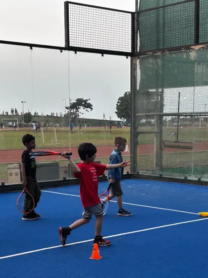 We focus on teaching the correct form from day one. In this shot, you can see young players practicing their swing technique under the watchful eye of a coach on our vibrant blue courts.