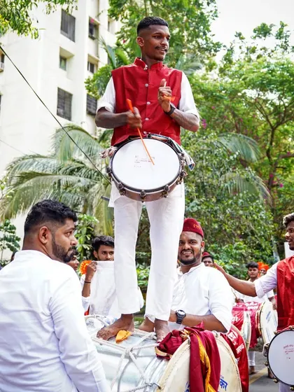 A unique perspective on the dhol performance. This performer stands atop a larger drum, showcasing the trust and coordination within the dhol-tasha group.