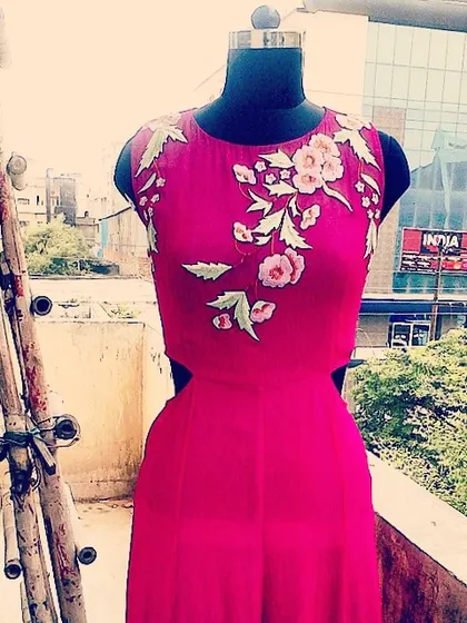 A vibrant pink jumpsuit with side cut-outs, displayed on a mannequin. The bodice is adorned with multi-tonal floral embroidery, making it a bold and fashionable choice for any party.
