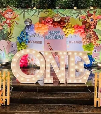 A premium jungle-themed first birthday setup with lighted arches and a variety of 3D animal props. The "ONE" marquee letters are a central feature of the stage.