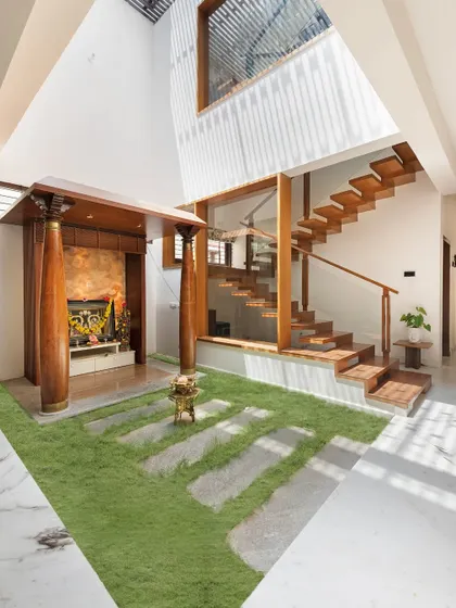 A view of the second courtyard, which houses the pooja mandapam. The design combines traditional wooden pillars with a modern floating staircase and a grass floor, blending cultural heritage with contemporary architecture.