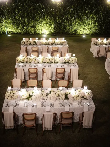 An aerial view of the formal dinner setup on the lawn. The symmetrical arrangement of the tables, each with its own floral runner and lamps, creates a powerful and organized visual.