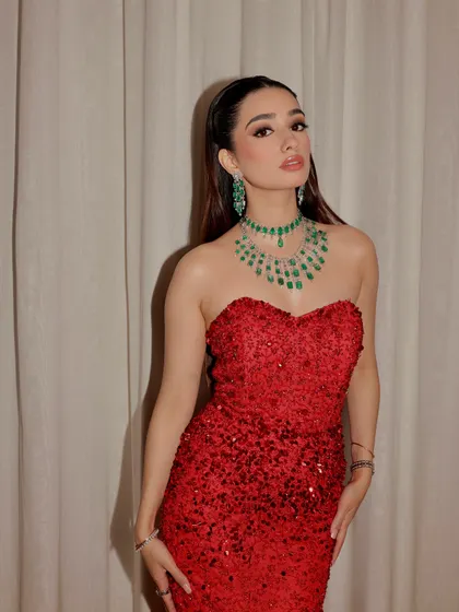 A fiery red gown for a glamorous evening. The makeup is bold and confident, with a wet-look ponytail and a stunning emerald necklace.