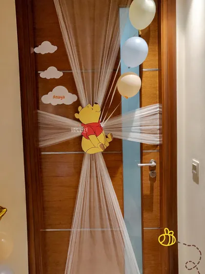 A whimsical Winnie the Pooh door decoration to welcome guests to Anaya's first birthday party. The sheer curtain with cloud cutouts and Pooh bear created a magical entrance.