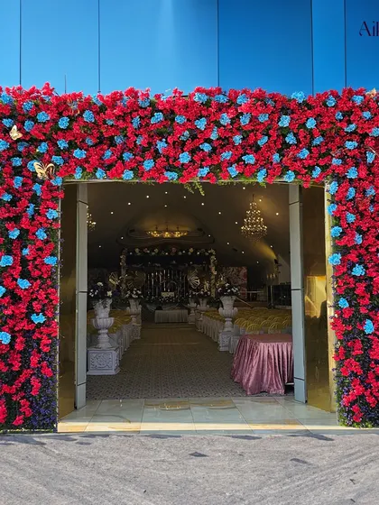 The grand entrance to the butterfly-themed event. A massive arch of red and blue flowers welcomes guests into the whimsical celebration.