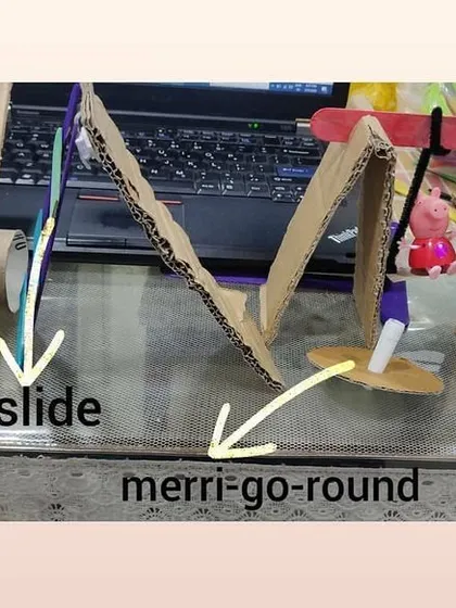 A detailed view of the cardboard playground, with labels pointing out the see-saw, slide, merry-go-round, and swing.