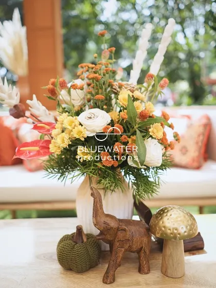 A beautiful floral arrangement in a terracotta pot, accented with a carved wooden elephant and mushroom.