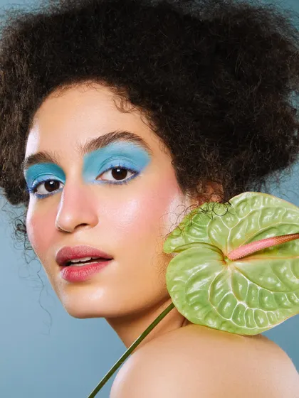 A vibrant floral-inspired look with a bold block of blue eyeshadow, contrasted with a fresh green anthurium flower.
