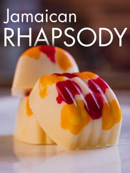 Our Jamaican Rhapsody pralines carry red and yellow details across a pale shell, shown here in a close-up.