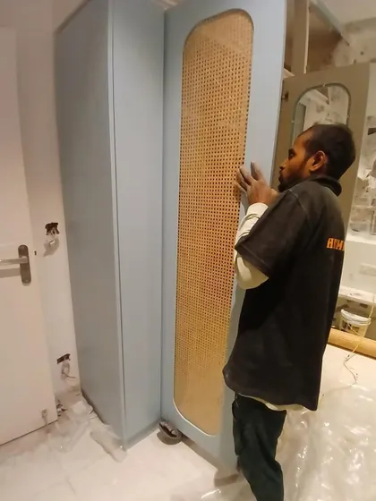 A perfect fit. One of our team members carefully installs a custom-made wardrobe door featuring a beautiful pastel blue finish and a natural cane panel.