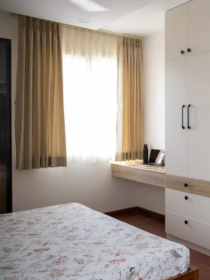 A functional and clean bedroom design with a built-in desk under the window. The automated curtains make it easy to control glare on the laptop screen without having to get up from the workspace.