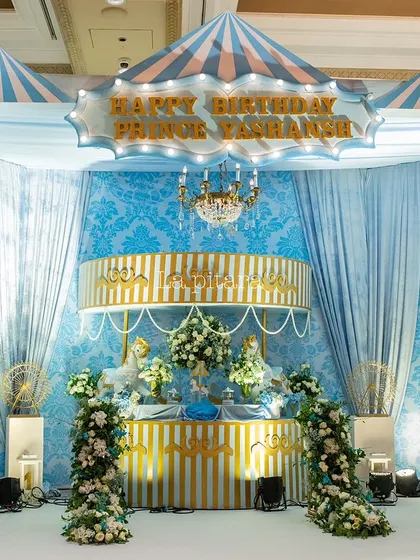 The stage for the carousel-themed birthday was designed to look like a vintage circus tent, with blue and white striped canopies and elegant draping. The "Happy Birthday" sign was lit up like a classic marquee.
