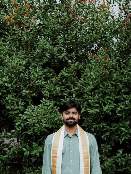 A handsome portrait of the groom standing against a lush green backdrop.