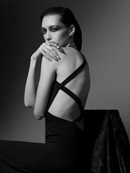 A classic black and white fashion portrait. The dramatic lighting, cross-back dress, and the model's intense gaze create a timeless and powerful image.