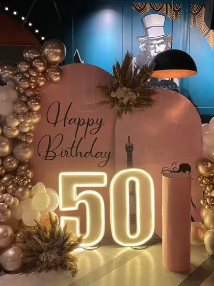 A closer look at the elegant 50th birthday decor. The warm glow from the neon numbers and the metallic sheen of the rose gold balloons create a warm and inviting atmosphere.