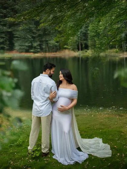 A serene portrait by the lake. The couple looks at each other, framed by the calm water and green forest, creating a peaceful and romantic scene.