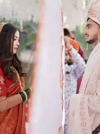 An intimate moment between the bride and groom during the 'antarpat' ceremony. This candid shot captures the emotion of the wedding, with the bride looking elegant in her orange and red saree.
