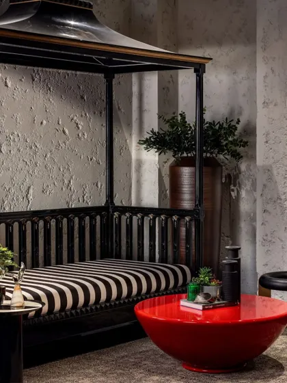 This seating nook in the basement of the House of Two Worlds features a custom canopy bed, textured walls, and a bold red coffee table. The material choices create a distinct and immersive character, setting it apart from the home's primary living spaces.