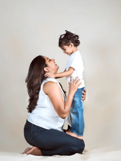 A mother kneels, looking up at her daughter with a huge smile. This simple pose creates a powerful image of a mother's adoration for her child.