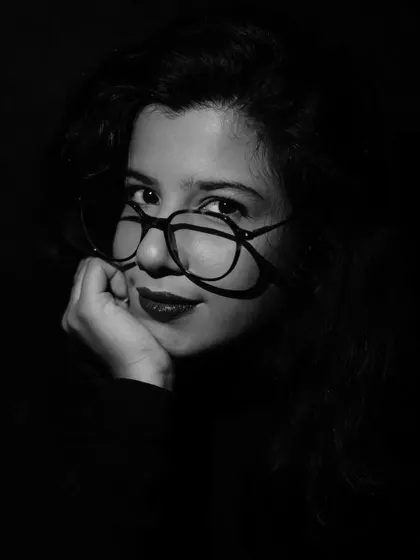 A soft, smiling portrait in a dramatic low-key light. The contrast between the dark setup and the gentle expression makes the image intriguing.