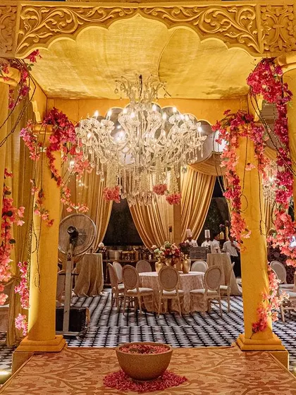 An entrance to the dining area, framed by golden pillars wrapped in pink flowers and topped with a sparkling chandelier. This creates a grand and welcoming transition for guests.