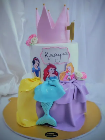 A Disney Princess dream cake for a first birthday. This two-tier design features Snow White, Ariel, and Rapunzel, with their iconic dresses recreated in fondant, all topped with a princess crown.
