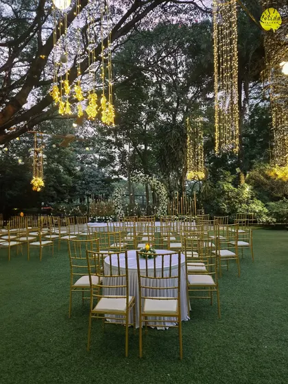An evening view of our lawn set up for a wedding, with tables arranged for guests under a canopy of trees adorned with beautiful, glowing lanterns.