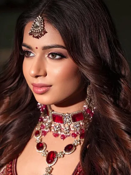 A close-up profile shot. The eye makeup is a beautiful blend of soft browns with a hint of purple, perfectly complementing the red outfit.