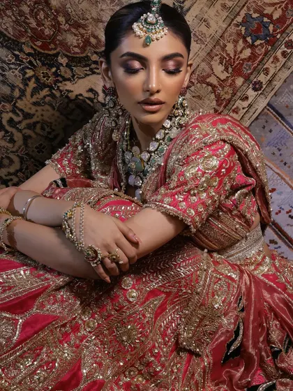 The rich textures of the carpet background complement the luxurious velvet and embroidery of the bridal lehenga.