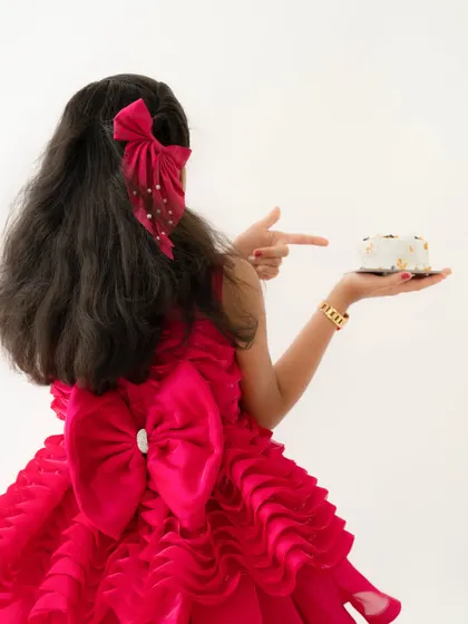 A creative shot from behind, showing off the beautiful bow on her dress as she points to her birthday cake.