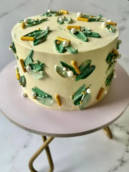 An abstract design using shades of green buttercream, applied with a palette knife technique. The cake is finished with edible pearls and gold sprinkles for a modern, artistic feel.