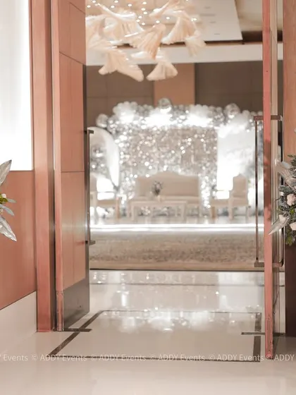 This metallic floral gate provides a glimpse into the glamorous celebration within. The modern silver frames adorned with white floral arrangements create a chic and sophisticated entrance to the main event hall.