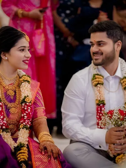 The couple sits together during their engagement ceremony, sharing a sweet look, adorned with beautiful garlands.